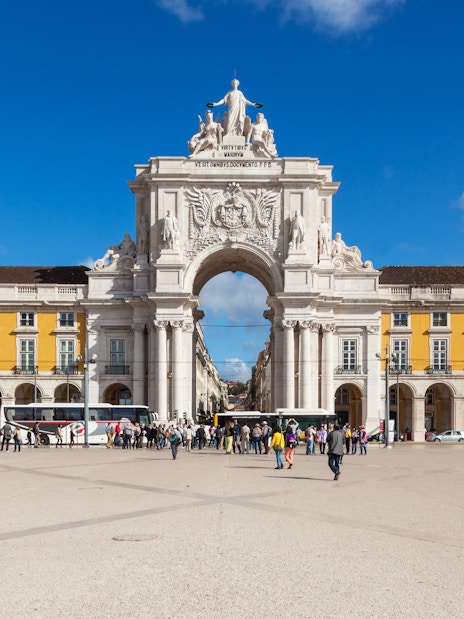 Rua Augusta Arch in Lisbon with people walking in the plaza.