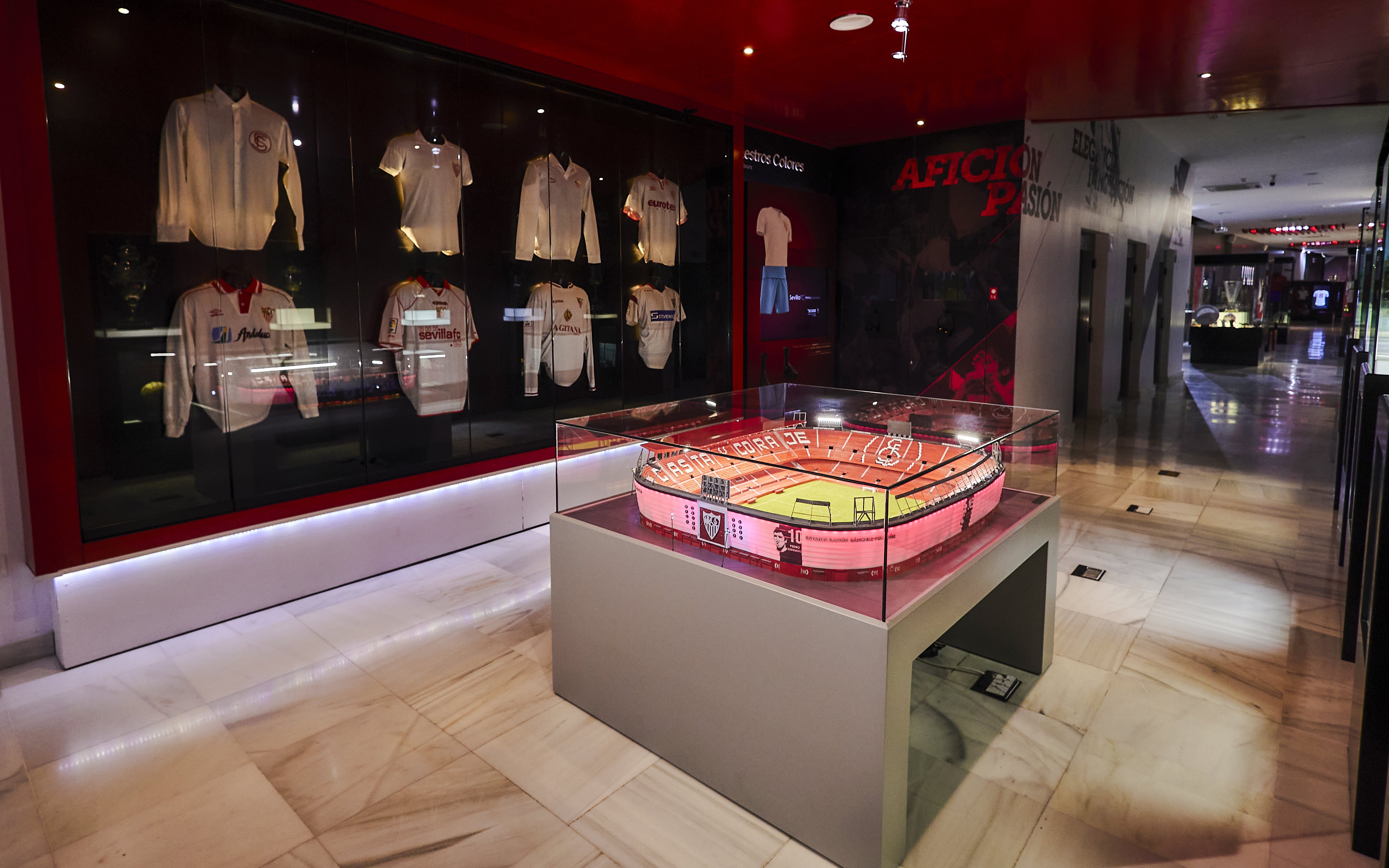 Scale model of Estadio Ramón Sánchez Pizjuán displayed in a museum with Sevilla FC jerseys.