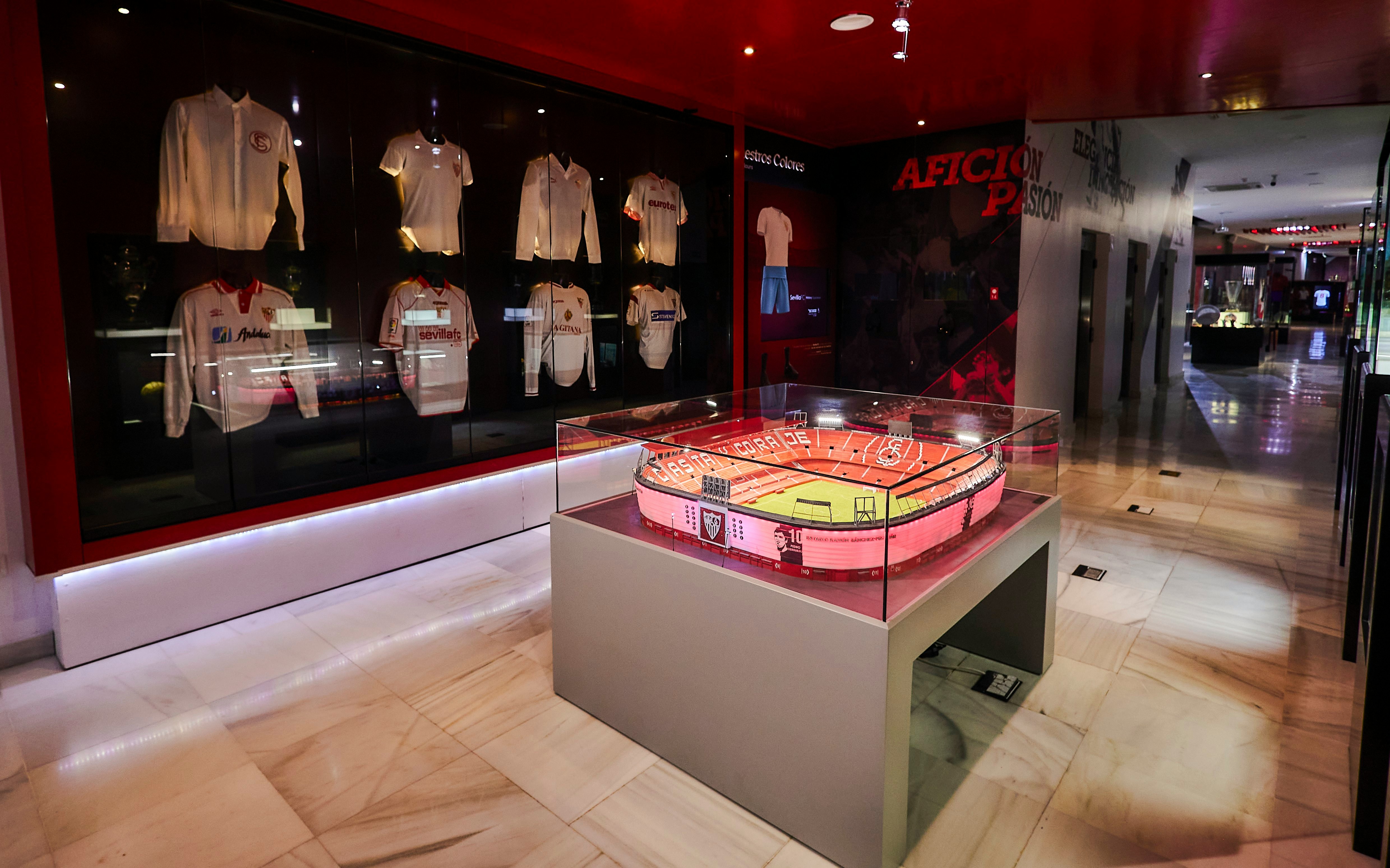 Scale model of Estadio Ramón Sánchez Pizjuán displayed in a museum with Sevilla FC jerseys.