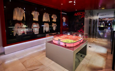 Scale model of Estadio Ramón Sánchez Pizjuán displayed in a museum with Sevilla FC jerseys.