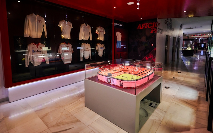 Scale model of Estadio Ramón Sánchez Pizjuán displayed in a museum with Sevilla FC jerseys.