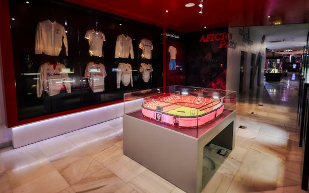Scale model of Estadio Ramón Sánchez Pizjuán displayed in a museum with Sevilla FC jerseys.