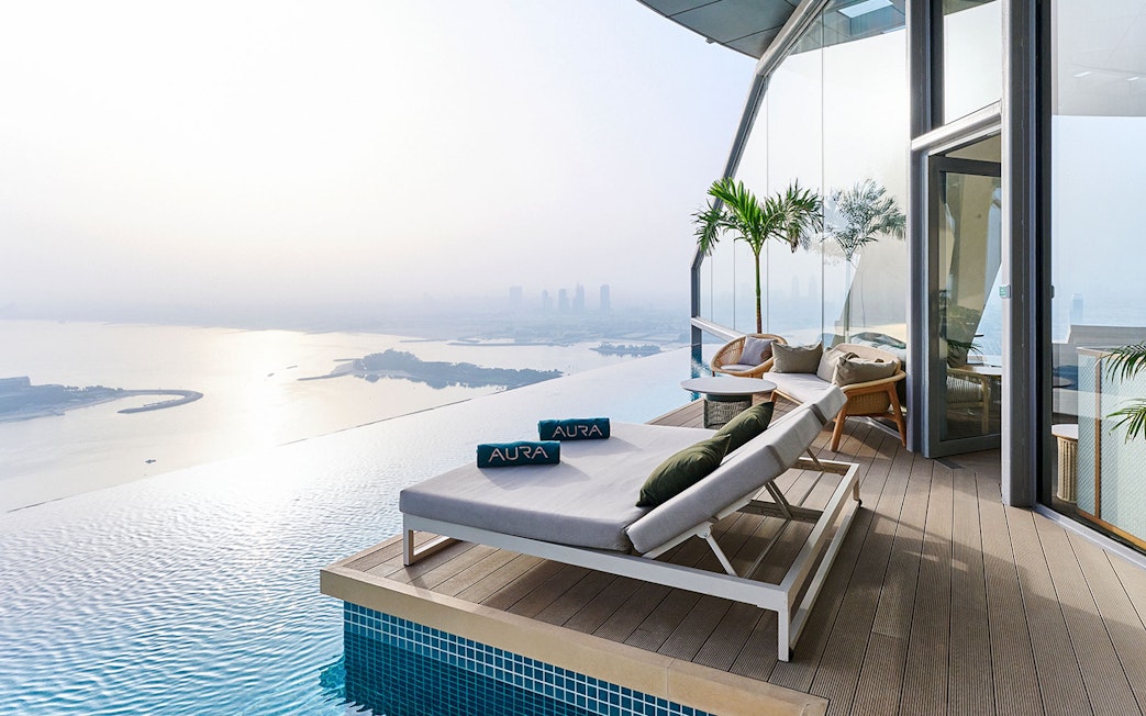 Sun loungers by the infinity pool at Rise at AURA Sky Pool, overlooking the city skyline.