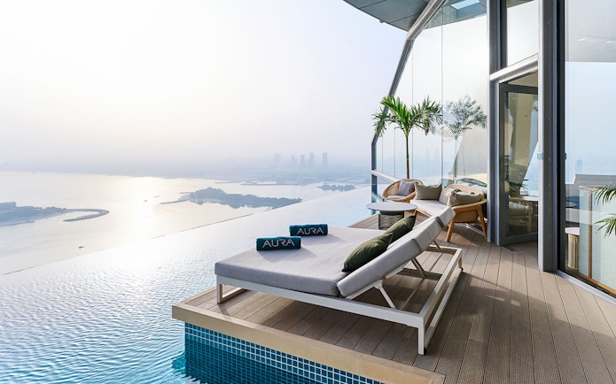Sun loungers by the infinity pool at Rise at AURA Sky Pool, overlooking the city skyline.