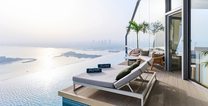 Sun loungers by the infinity pool at Rise at AURA Sky Pool, overlooking the city skyline.