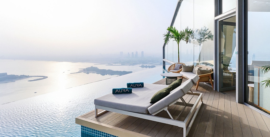 Sun loungers by the infinity pool at Rise at AURA Sky Pool, overlooking the city skyline.