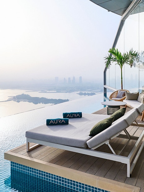 Sun loungers by the infinity pool at Rise at AURA Sky Pool, overlooking the city skyline.