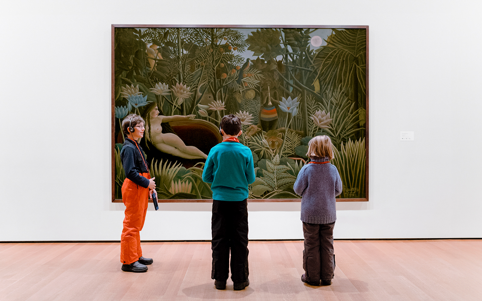 Children viewing a jungle-themed painting in an art museum.