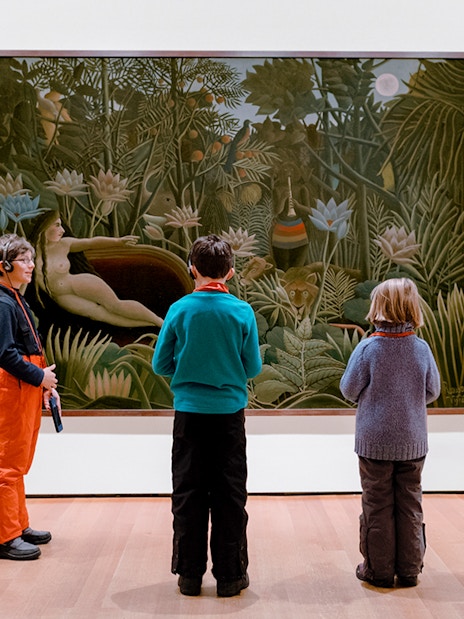 Children viewing a jungle-themed painting in an art museum.