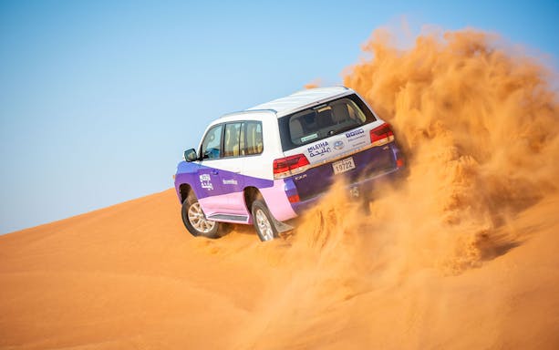 SUV driving through sand dunes on Mleiha tour with Fossil Rock visit.
