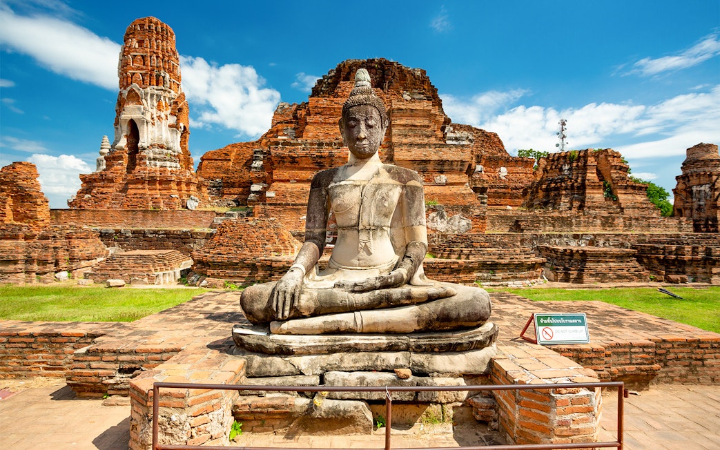 Seated Buddha statue at Ayutthaya Historical Park, Thailand, with ancient brick ruins.