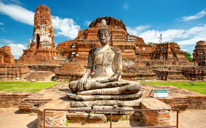 Seated Buddha statue at Ayutthaya Historical Park, Thailand, with ancient brick ruins.