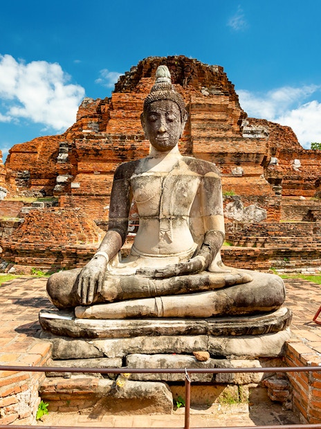 Seated Buddha statue at Ayutthaya Historical Park, Thailand, with ancient brick ruins.
