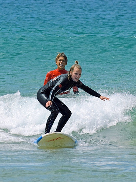 Group surf lesson with instructor guiding a student on a wave.