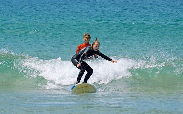 Group surf lesson with instructor guiding a student on a wave.