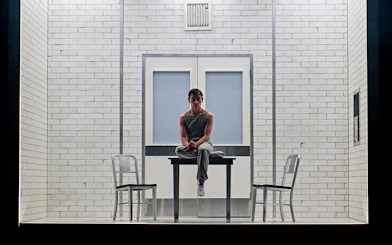 Young person sitting on a table in a tiled room, part of Stranger Things: The First Shadow.