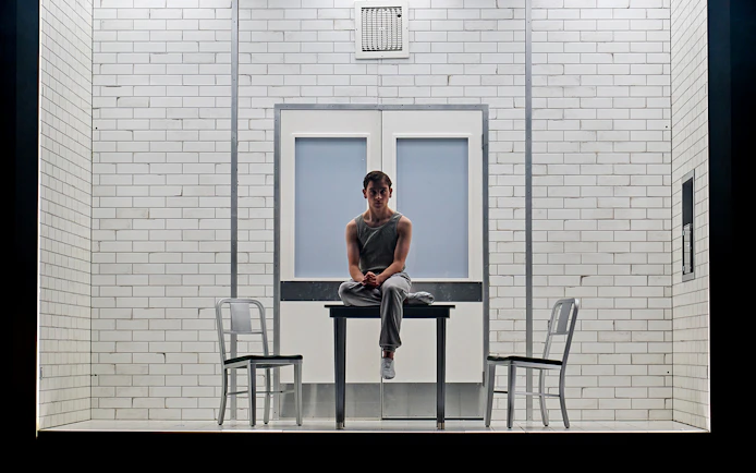 Young person sitting on a table in a tiled room, part of Stranger Things: The First Shadow.