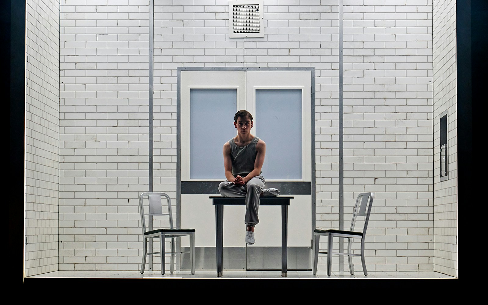 Young person sitting on a table in a tiled room, part of Stranger Things: The First Shadow.