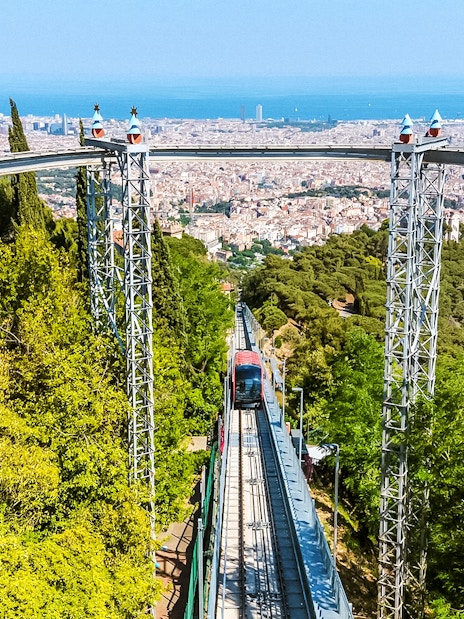 Funicular ascending Tibidabo Amusement Park with Barcelona cityscape in the background.