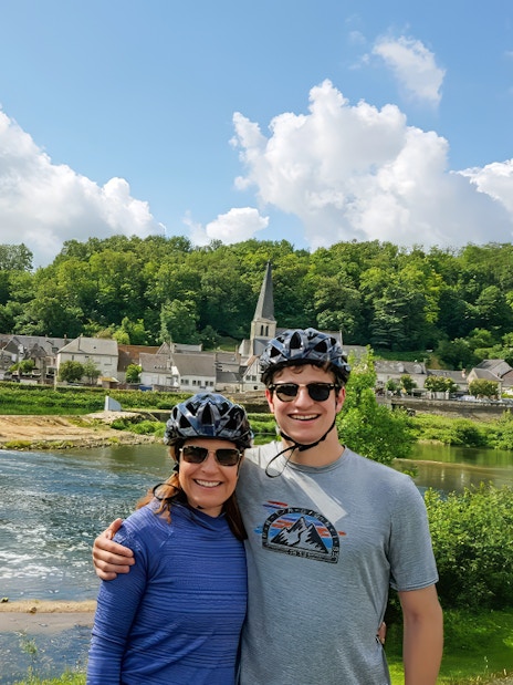 Cyclists by river with village and church in background, full day e-bike tour to Chambord.