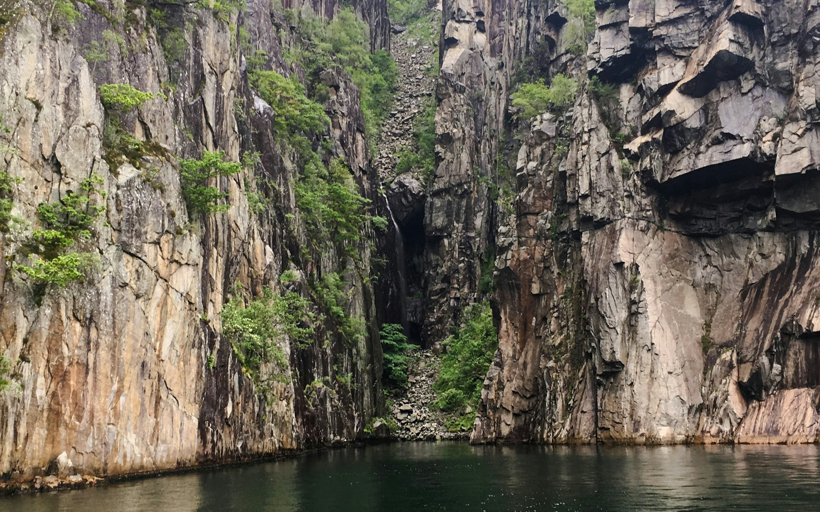 Fantahåla cave entrance surrounded by steep cliffs and greenery, Stavanger, Norway.