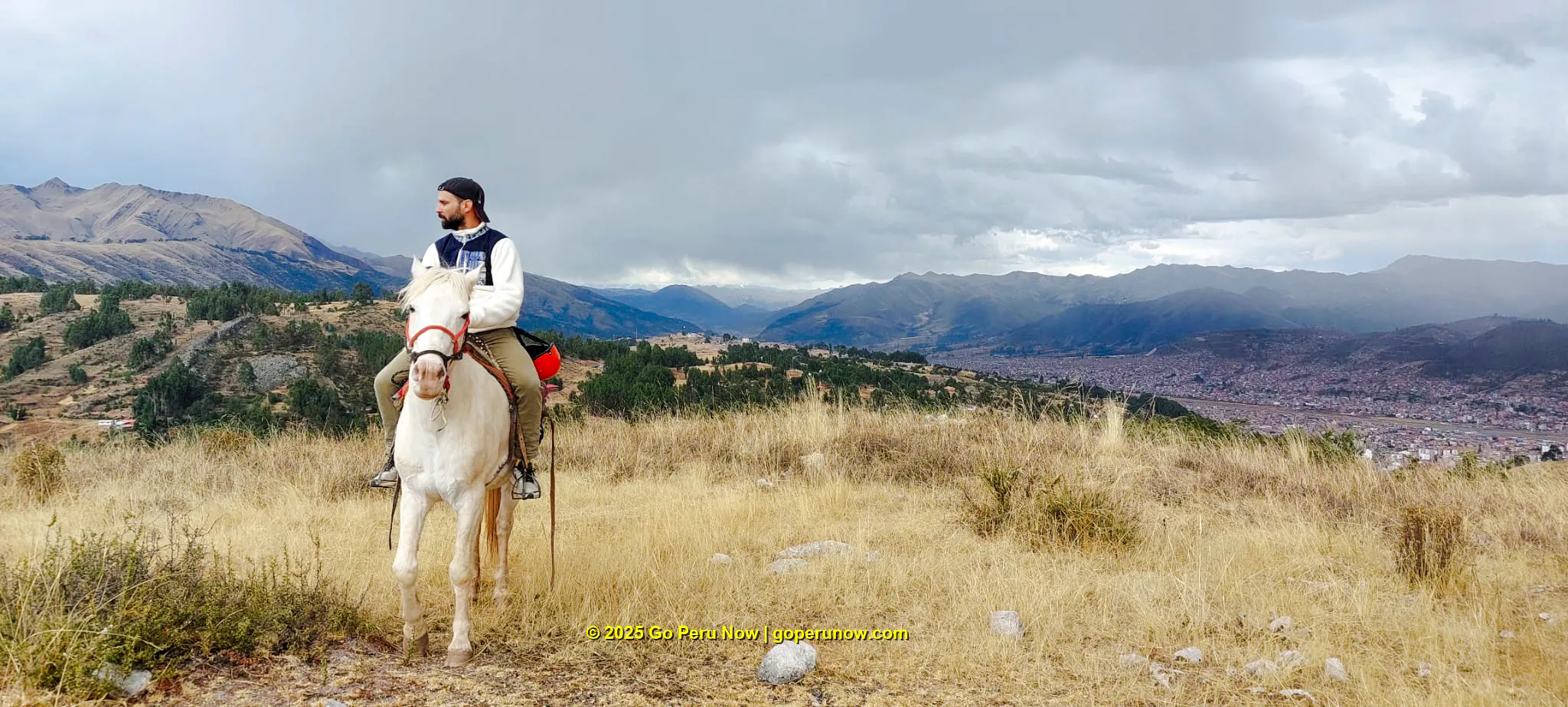 Horseback rider overlooking Cusco cityscape and mountains, Peru.