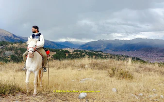 Horseback rider overlooking Cusco cityscape and mountains, Peru.