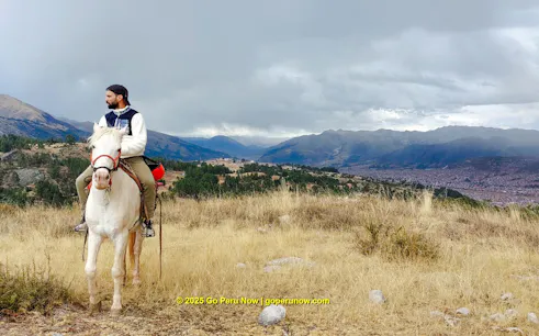Horseback rider overlooking Cusco cityscape and mountains, Peru.