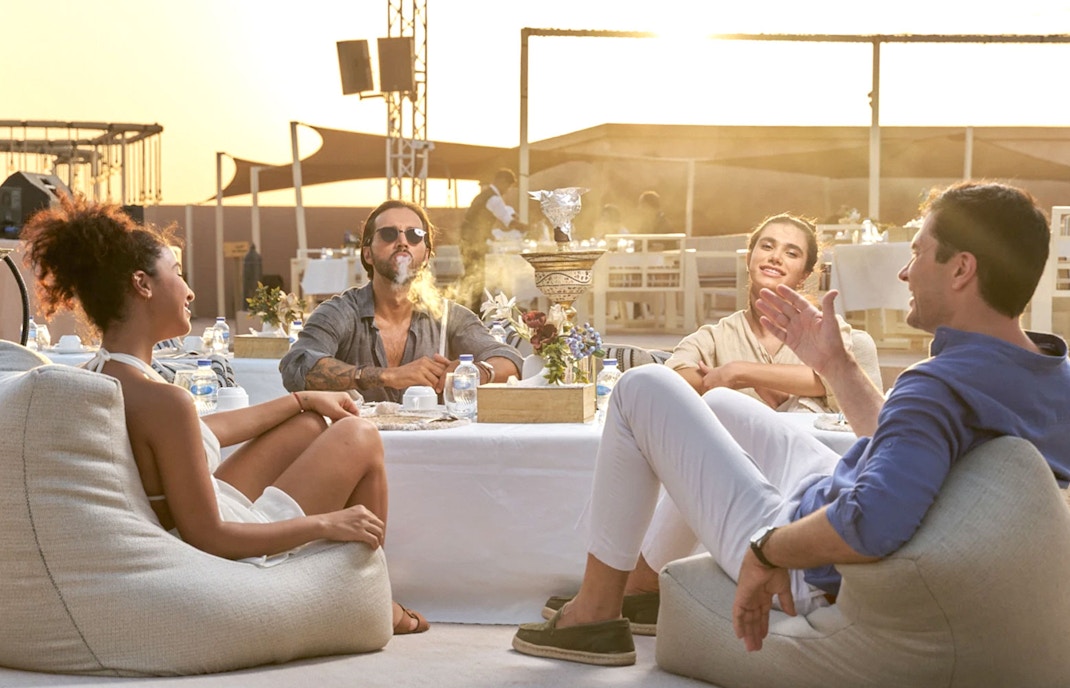 Group enjoying premium seating with food and hookah in Dubai desert setting.