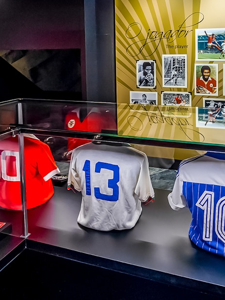 Benfica Stadium museum display with historic football jerseys and player photos.