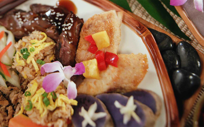 Traditional Hawaiian luau plate with grilled meat, rice, and tropical garnishes at Smiths Family Garden Luau.