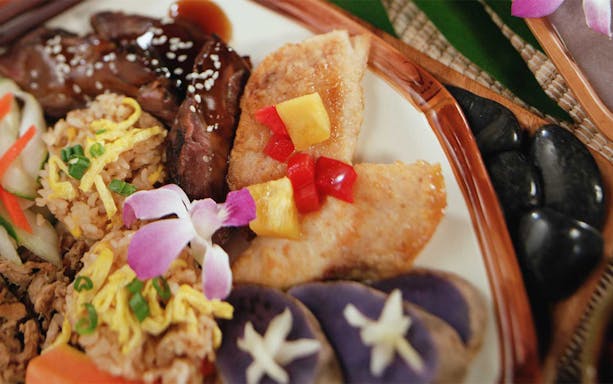 Traditional Hawaiian luau plate with grilled meat, rice, and tropical garnishes at Smiths Family Garden Luau.
