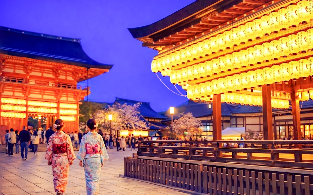 Nighttime view of Yasaka Shrine in Kyoto with illuminated lanterns and visitors in traditional attire.