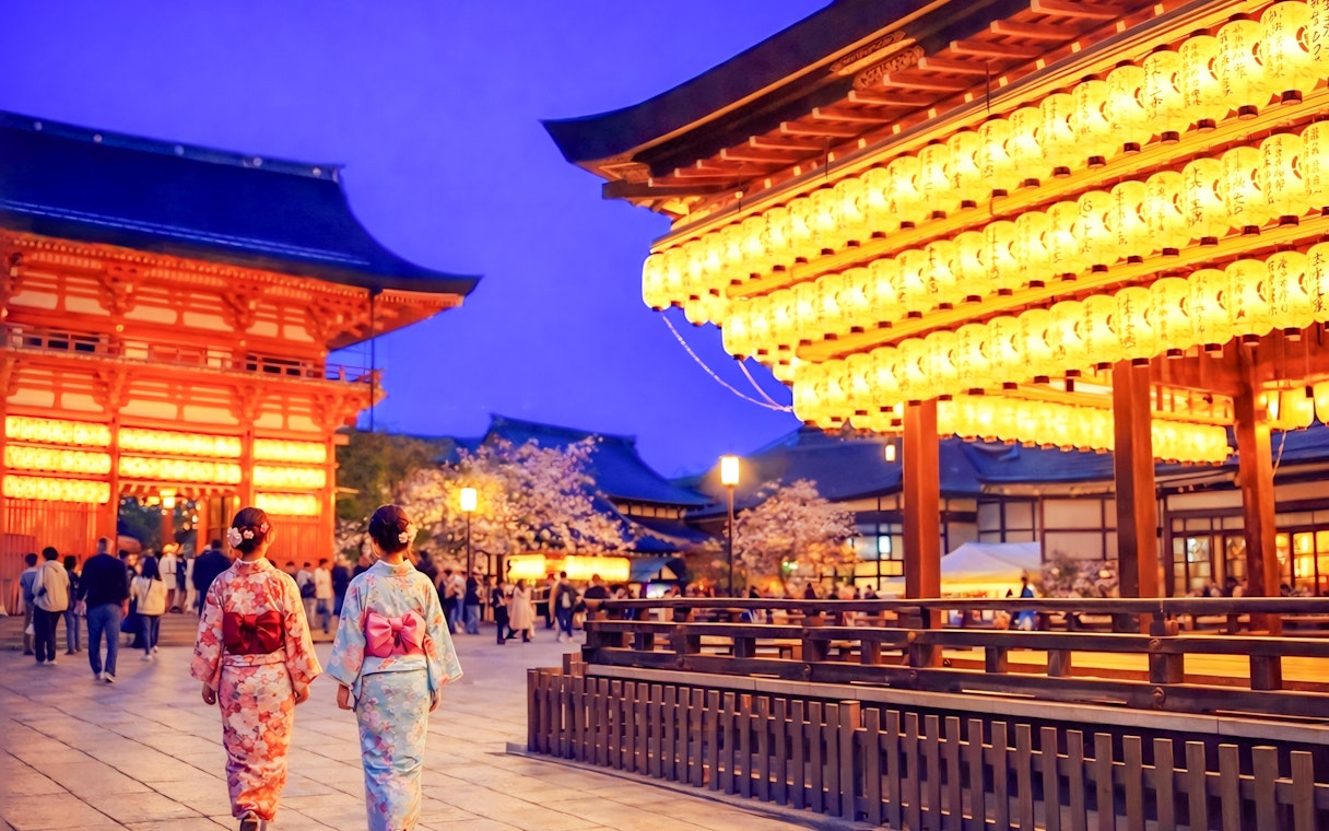 Nighttime view of Yasaka Shrine in Kyoto with illuminated lanterns and visitors in traditional attire.