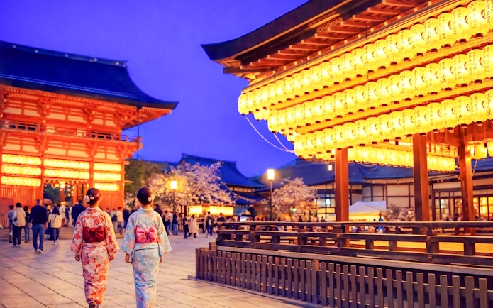 Nighttime view of Yasaka Shrine in Kyoto with illuminated lanterns and visitors in traditional attire.