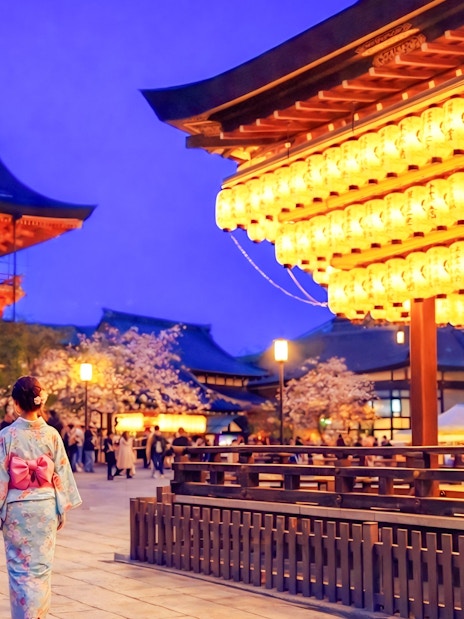 Nighttime view of Yasaka Shrine in Kyoto with illuminated lanterns and visitors in traditional attire.