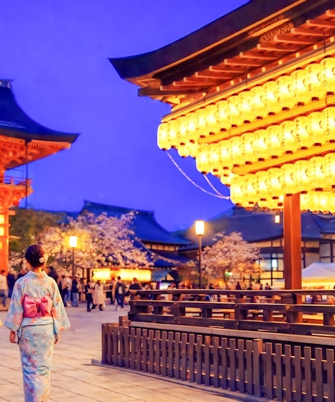 Nighttime view of Yasaka Shrine in Kyoto with illuminated lanterns and visitors in traditional attire.