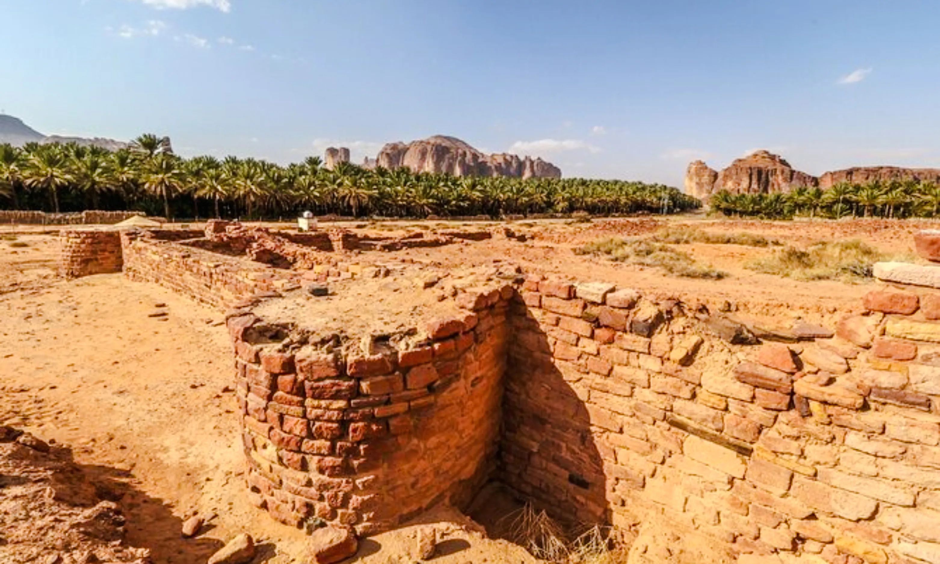 Ancient ruins at Hegra with palm trees and rocky landscape in AlUla, Saudi Arabia.