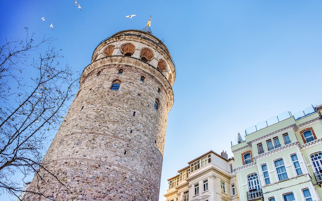 Galata Tower exterior with nearby buildings in Istanbul under a clear blue sky.