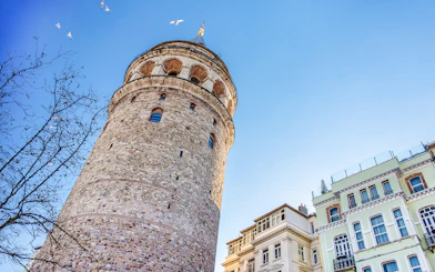 Galata Tower exterior with nearby buildings in Istanbul under a clear blue sky.