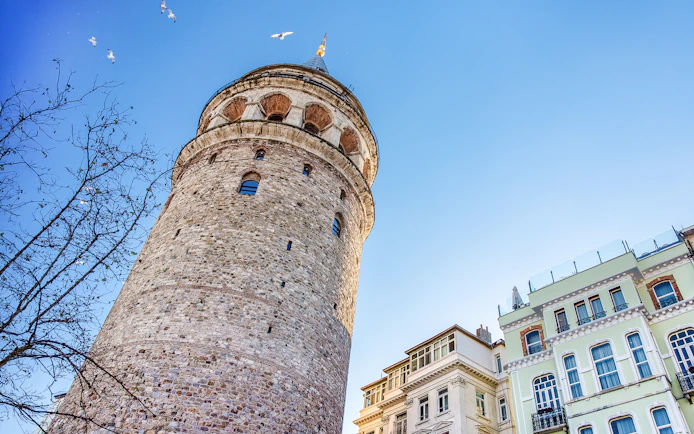 Galata Tower exterior with nearby buildings in Istanbul under a clear blue sky.