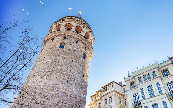 Galata Tower exterior with nearby buildings in Istanbul under a clear blue sky.