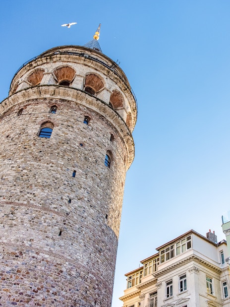 Galata Tower exterior with nearby buildings in Istanbul under a clear blue sky.