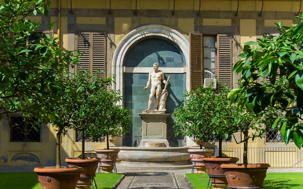 Statue in the garden of Palazzo Medici Riccardi, Florence, surrounded by potted trees.