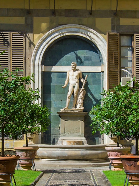 Statue in the garden of Palazzo Medici Riccardi, Florence, surrounded by potted trees.