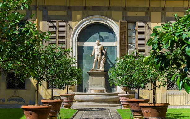 Statue in the garden of Palazzo Medici Riccardi, Florence, surrounded by potted trees.