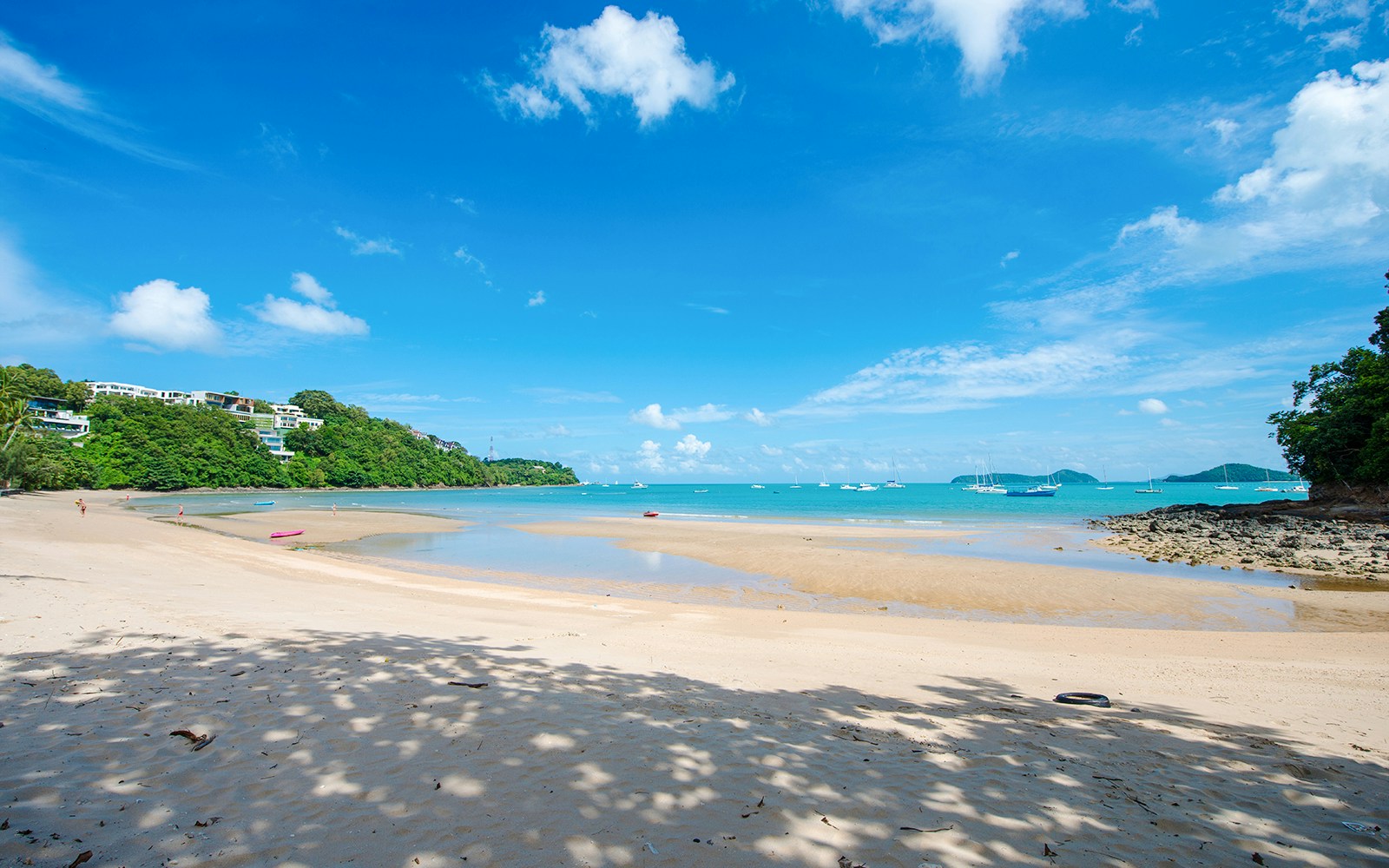 Ao Yon Beach in Phuket with clear blue water, sandy shore, and boats in the distance.