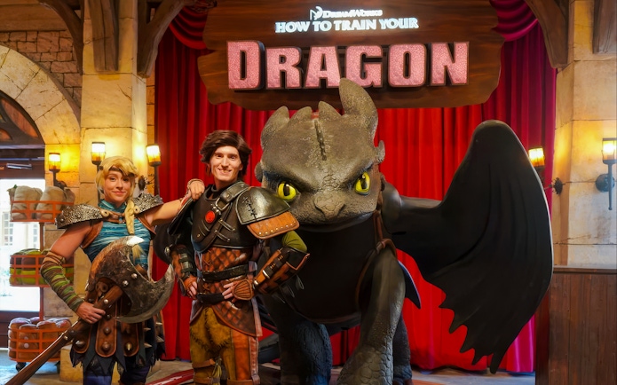 Hiccup and Astrid with Toothless at a How to Train Your Dragon event backdrop.