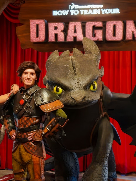Hiccup and Astrid with Toothless at a How to Train Your Dragon event backdrop.