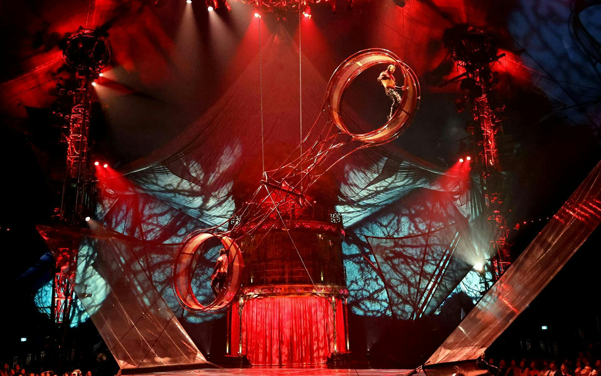 Performer on rotating wheel during Kooza stage show with dramatic lighting.